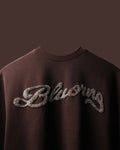Brown sweatshirt with 'Blvckng' text in rhinestones on a dark background