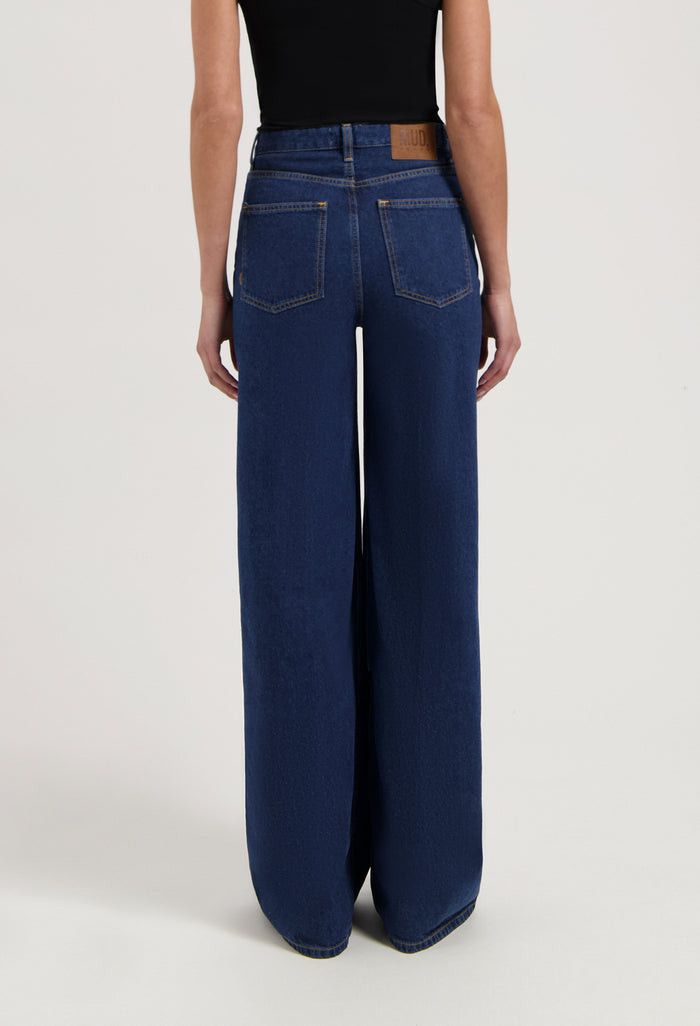 Wide-leg blue denim jeans from MUD Jeans made from organic cotton, shown from the rear, paired with a sleeveless black top.