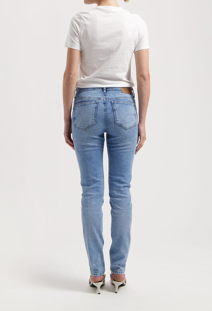 Back view of light blue denim jeans paired with a simple white T-shirt, worn by a model standing in heels.
