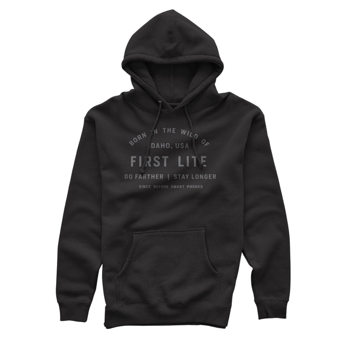 Black hoodie with gray text on the front saying 'Born in the wild of Idaho, USA, First Lite, Go farther | Stay longer, Since before smart phones', a drawstring hood, and a kangaroo pocket.