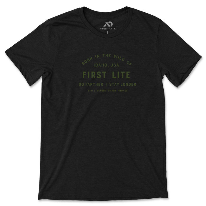Heather black t-shirt featuring olive green "FIRST LITE" branding and "BORN IN THE WILD OF IDAHO, USA" text on the chest.