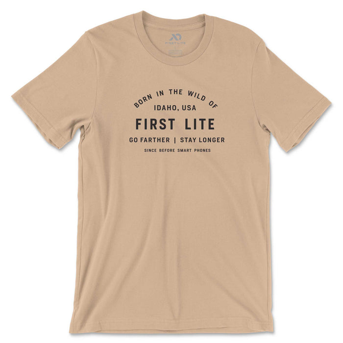 Tan t-shirt with black text that reads 'Born in the wild of Idaho, USA FIRST LITE GO FARTHER | STAY LONGER SINCE BEFORE SMART PHONES'.