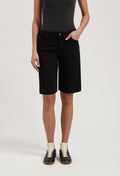 Black denim Bermuda shorts paired with a dark gray sleeveless top, worn with black and white sneakers.