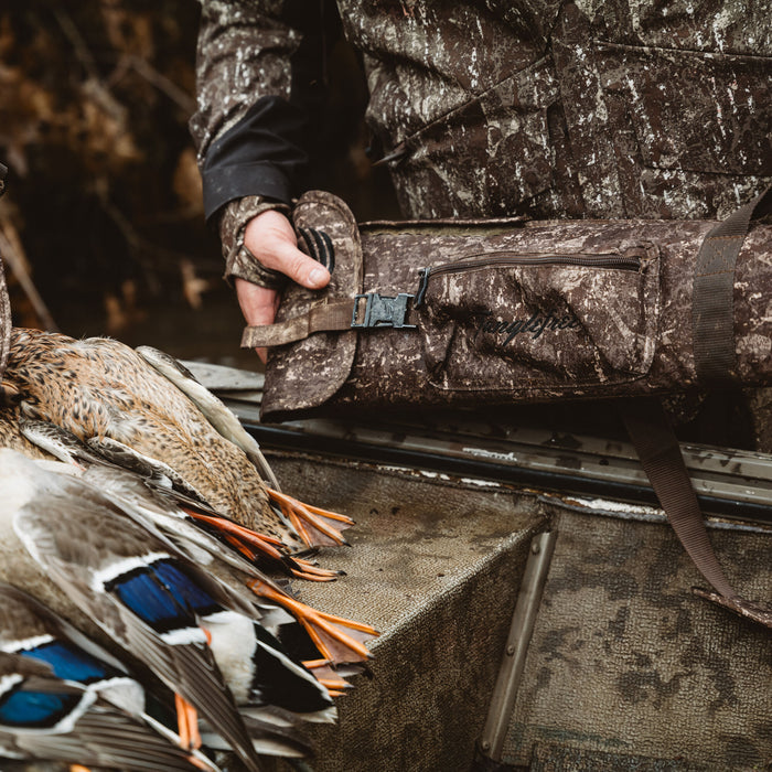 A person holds a brown and green camouflage Tanglefree gun bag with a visible buckle and zipper, next to several harvested ducks.
