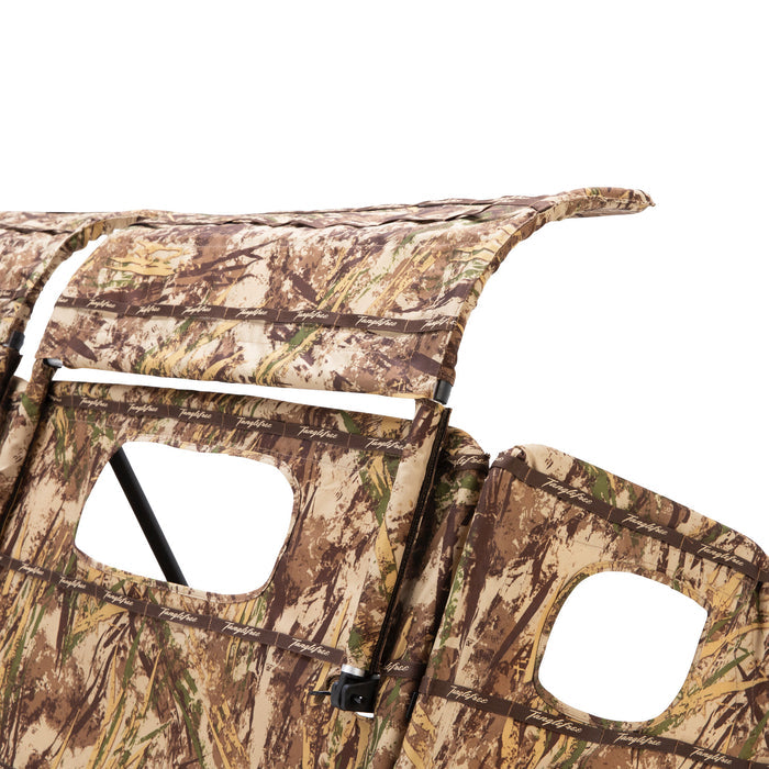 Close-up of a multi-panel camouflage hunting blind in brown, green, and tan, featuring observation cutouts and Tanglefree branded straps.
