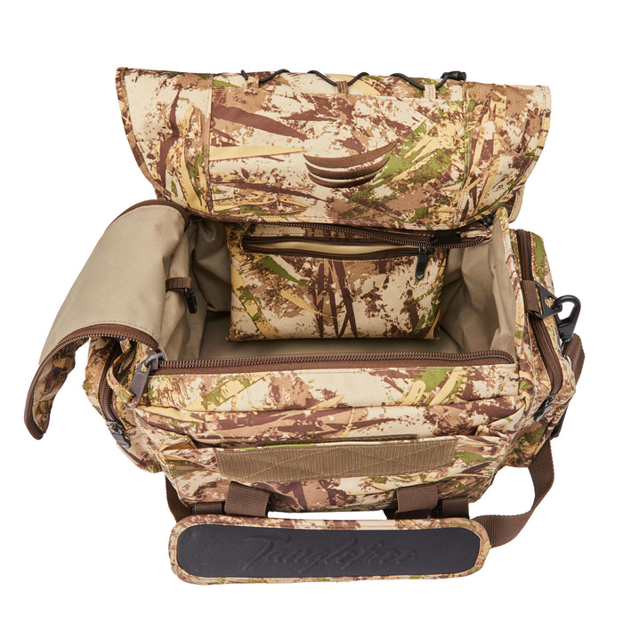 Open camouflage hunting gear bag in a brown, green, and beige pattern, revealing its interior with a matching zippered pouch and a shoulder strap pad embossed 'Tanglefree'.