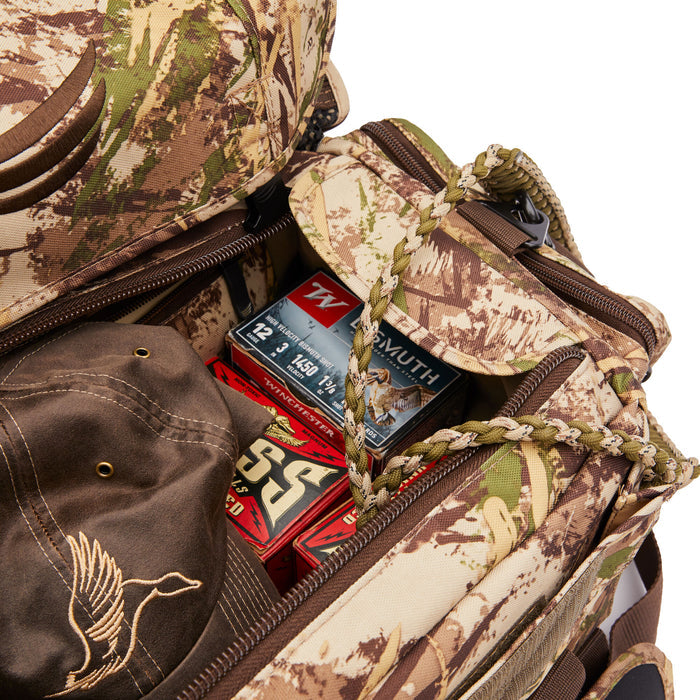 Open camouflage duffel bag filled with shotgun shell boxes and a brown hat embroidered with a flying duck.