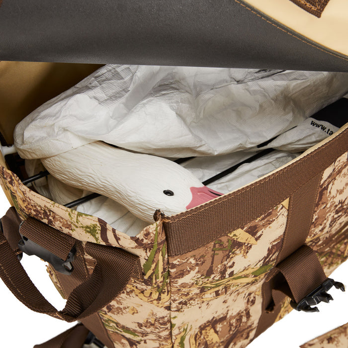 Open camouflage decoy bag containing white snow goose decoys, with one pink-beaked head visible.