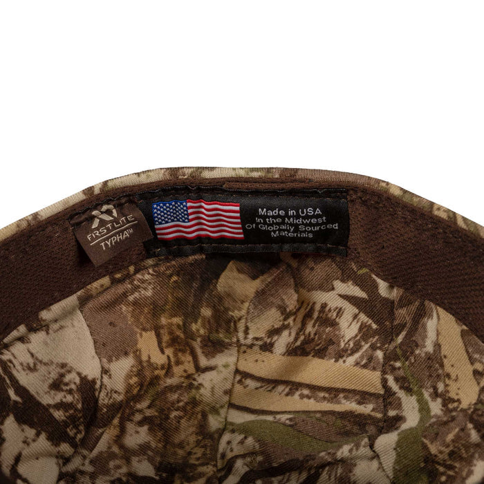 Inside view of a brown and tan camouflage cap, featuring a First Lite Typha brand label and a 'Made in USA' label with an American flag.