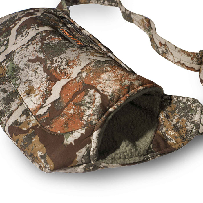 First Lite Fusion camouflage hand muff with a zippered pocket, fleece-lined opening, and shoulder strap.