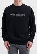 Sustainable MUD Jeans black sweater with "Make the Planet Cooler" slogan, paired with gray denim, ethical fashion choice.