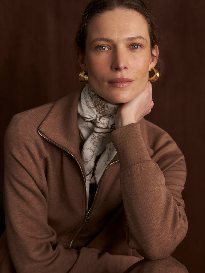 Golden Bronze Marl|Model standing facing forward with hands in pockets, wearing the Tyde Zip Through Sweat in golden bronze marl, featuring a two-way zip, knitted collar, and crafted from Varley’s signature DoubleSoft® fabric.