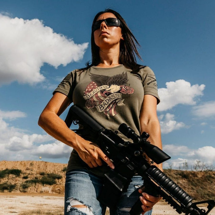 Person holding a rifle against a desert landscape with a blue sky.