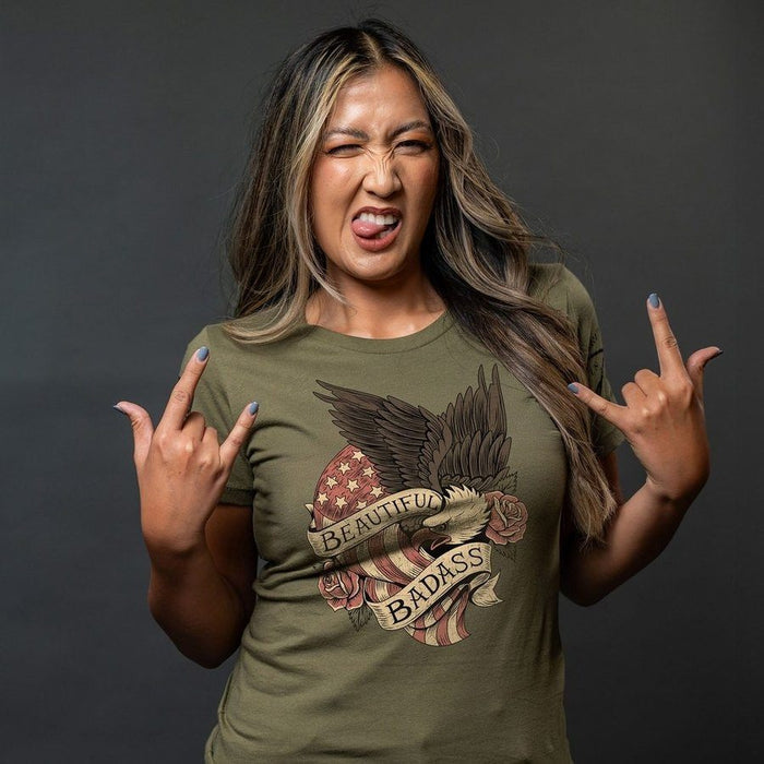 Woman wearing a green t-shirt with a graphic design and text, making a rock-on gesture against a dark background.