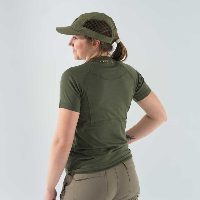 A woman wears an olive green First Lite short-sleeved t-shirt with raglan sleeves and a matching cap featuring mesh side panels.