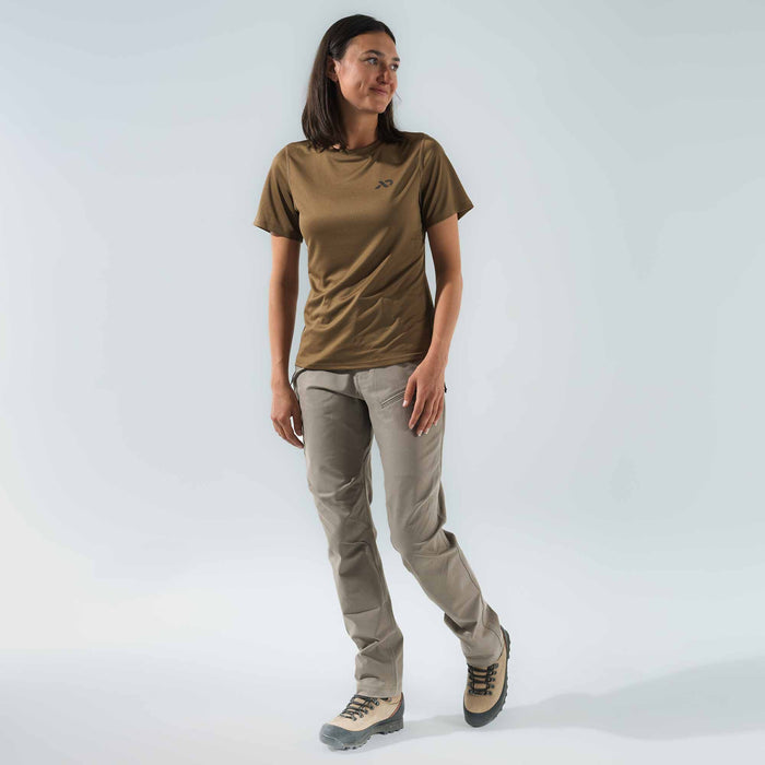 A woman wears an olive green short-sleeve t-shirt with a dark chest logo and Walnut outdoor pants with a zippered thigh pocket.